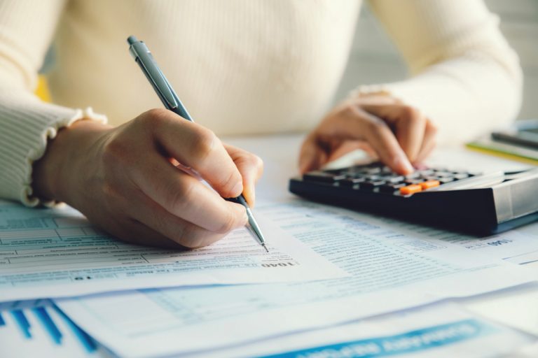 Pessoa anotando em papel contas feitas em uma calculadora sobre o valor venal do seu imóvel