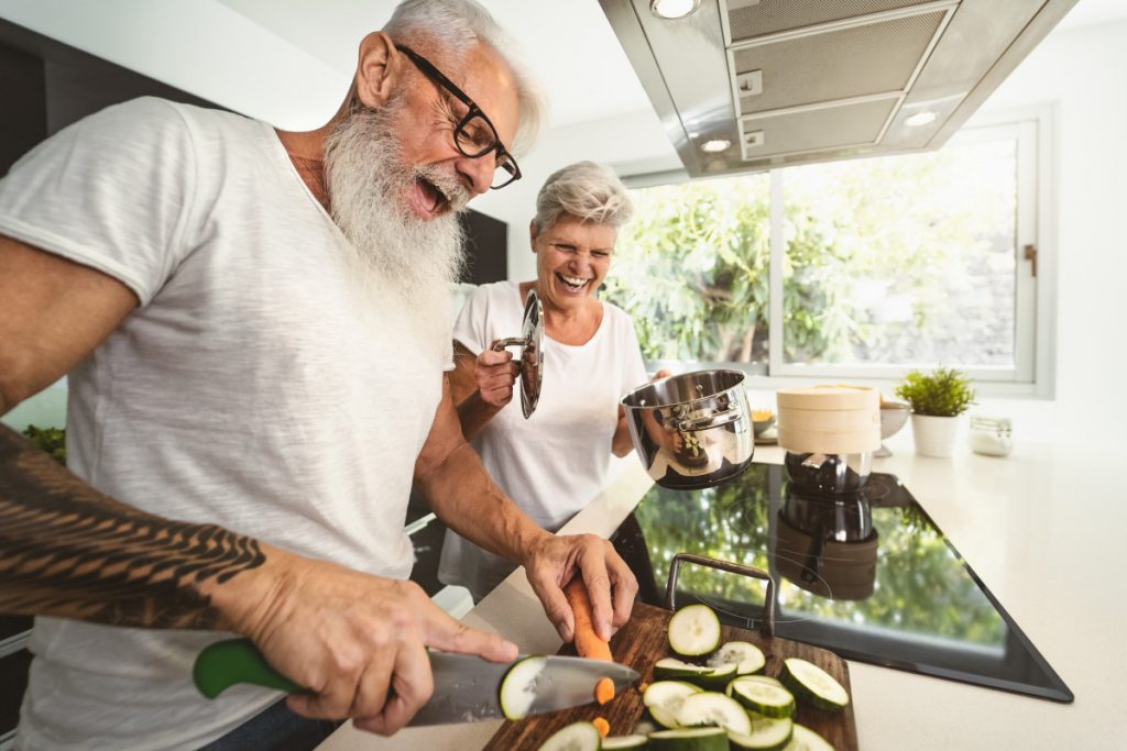 Casal de idosos cortando legumes no espaço gourmet de casa em almoço de família