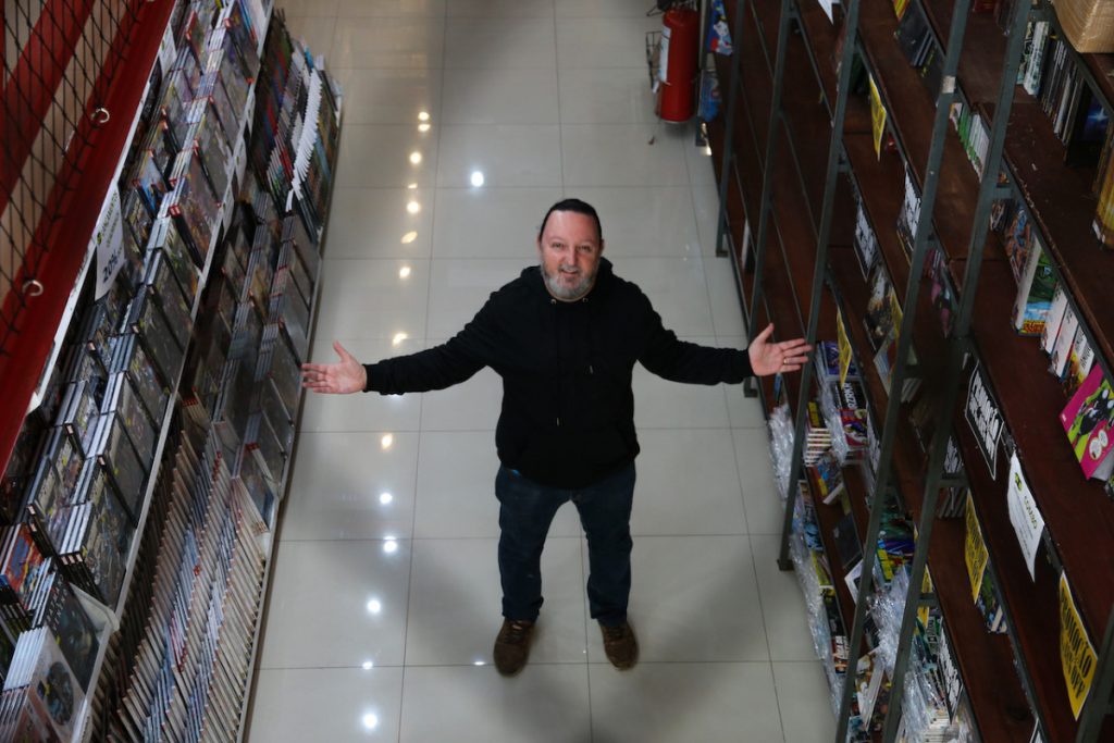 Um homem está de braços abertos dentro de sua livraria em São Paulo